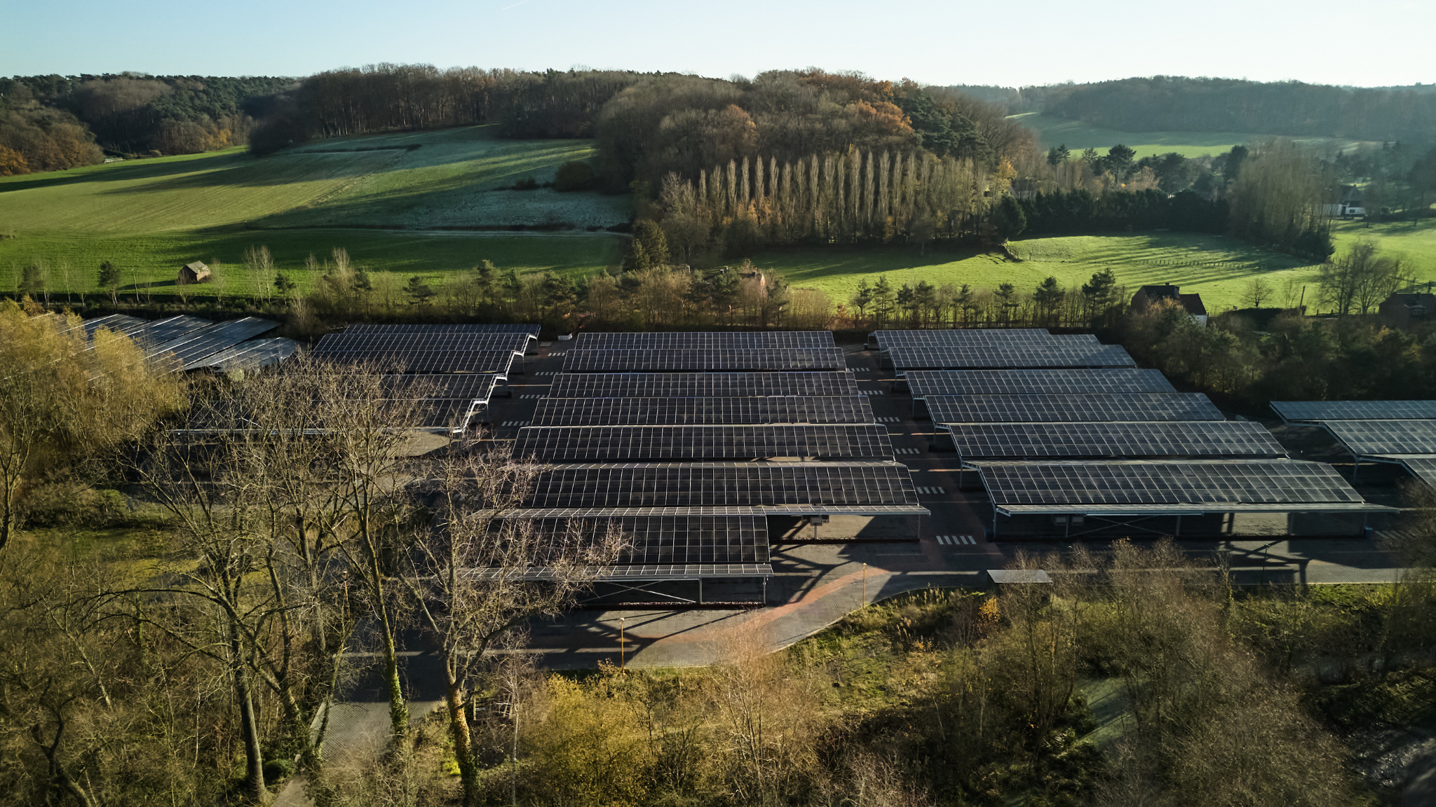 Aerial view of a solar farm in the countryside, showcasing rows of solar panels surrounded by green fields.